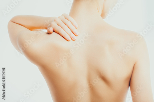 Slender, nude woman massages her neck and shoulders