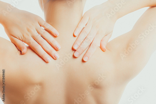 Slender, nude woman massages her neck and shoulders