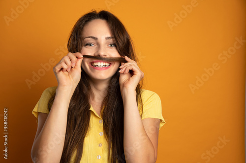 laughing young woman who makes a mustache with a lock of her hair on an orange background
