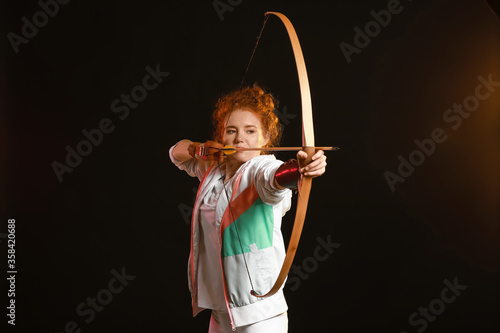 Beautiful female archer with bow on dark background Fototapeta