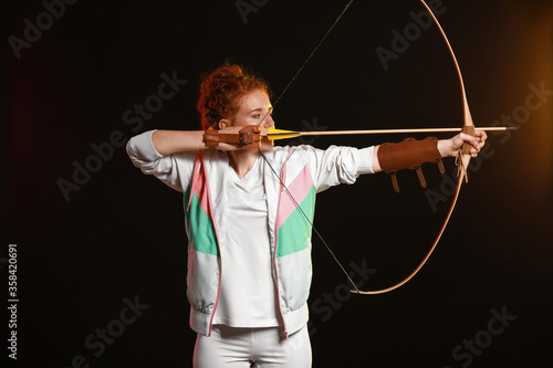Beautiful female archer with bow on dark background