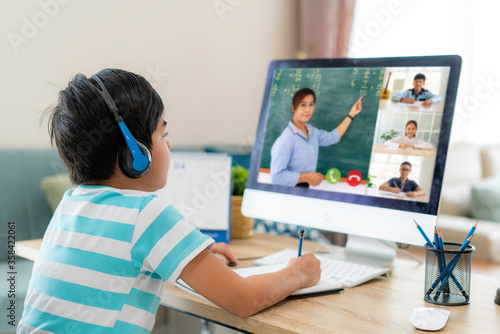 Asian boy student video conference e-learning with teacher and classmates on computer in living room at home. Homeschooling and distance learning ,online ,education and internet. photo