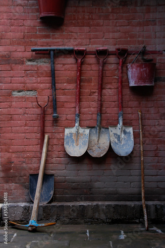 Set of tools (shovel, pick and bucket) hanging on a red brick wall