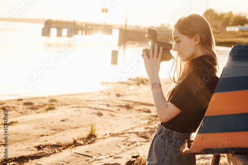 A beautiful stylish blonde walks with a retro film camera нipster casual against the sea rivers