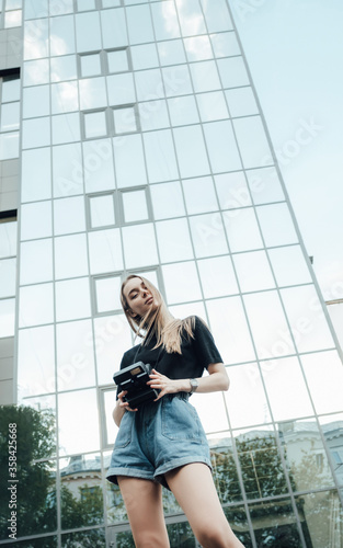 A beautiful stylish blonde walks with a film camera нipster casual 
against the background of a skyscraper