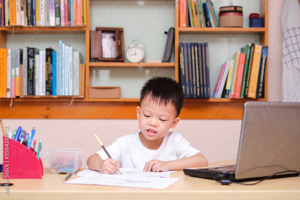 Asian little kid drawing and using laptop computer studying homework during his online lesson at home, Kindergarten closed during the Covid-19 health crisis, Distance learning, homeschooling concept Asian little kid drawing and using laptop computer studying homework during his online lesson at home, Kindergarten closed during the Covid-19 health crisis, Distance learning, homeschooling concept