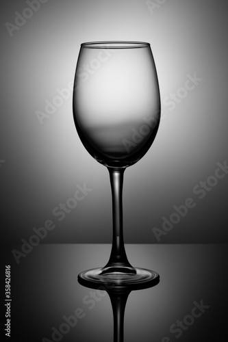 Transparent wine glass stands on black glossy glass, back spot illumination