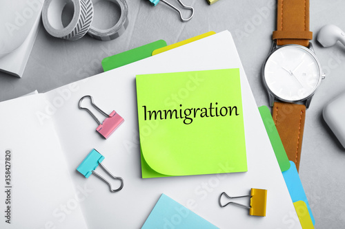 Note with word IMMIGRATION and stationery on grey grey table, flat lay photo