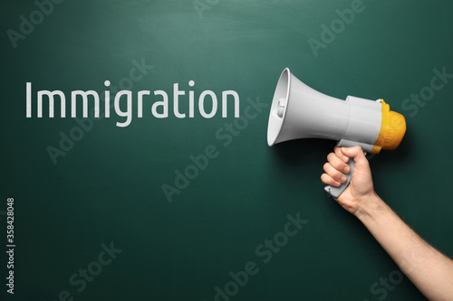 Man holding megaphone near chalkboard with word IMMIGRATION
