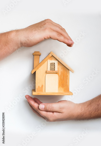 detail of male hands surrounding a small wooden house on white background
