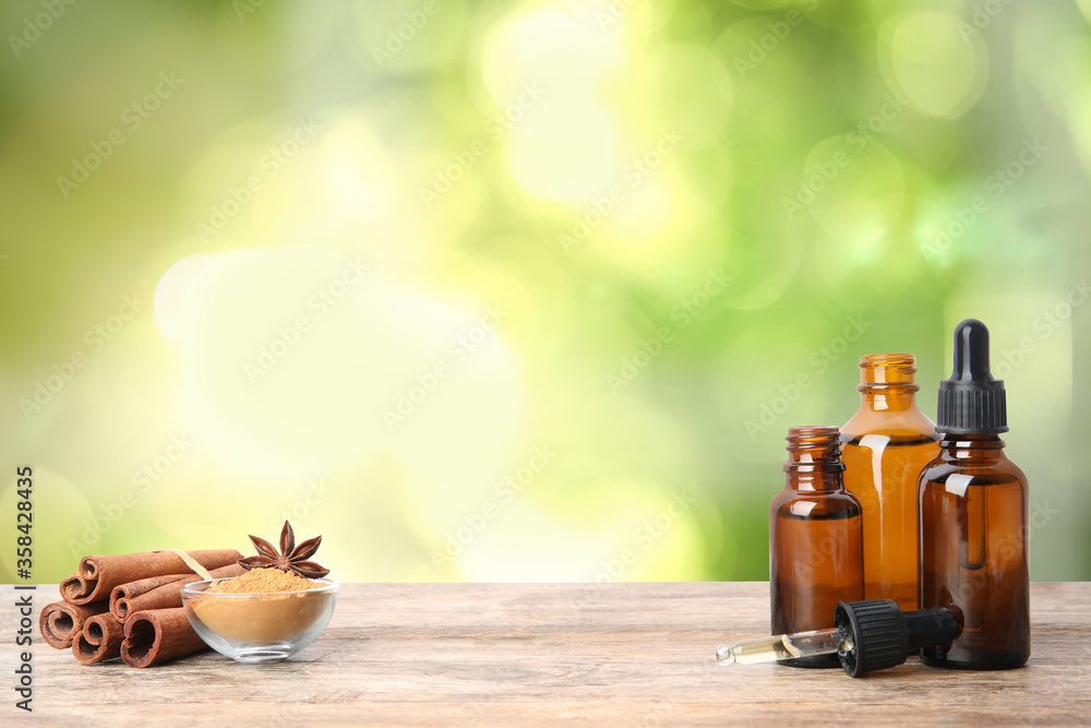 Bottles of essential oil, cinnamon sticks and powder on wooden table against blurred background. Space for text Bottles of essential oil, cinnamon sticks and powder on wooden table against blurred background. Space for text