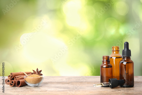 Bottles of essential oil, cinnamon sticks and powder on wooden table against blurred background. Space for text