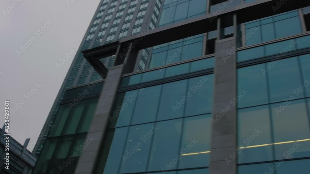 TORONTO, CANADA - MAY 14 2019 Angled tracking shot of window covered office buildings taken from street view. A stark city over an overcast sky. TORONTO, CANADA - MAY 14 2019 Angled tracking shot of window covered office buildings taken from street view. A stark city over an overcast sky.