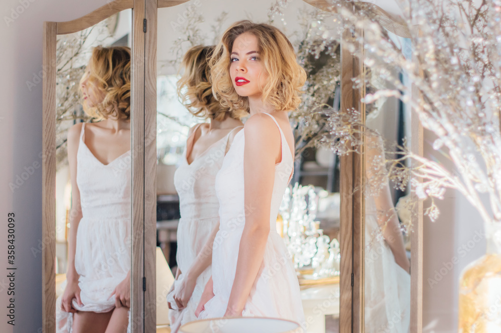 Fototapeta premium Beautiful blond girl with vintage make up and hairstyle staying near mirror
