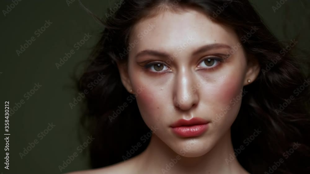 A beautiful young woman with long curly black hair, breast portrait, bare shoulders. Beautiful natural skin. Nude makeup. Red lips and graceful hands. Girl poses in studio against an olive background. A beautiful young woman with long curly black hair, breast portrait, bare shoulders. Beautiful natural skin. Nude makeup. Red lips and graceful hands. Girl poses in studio against an olive background.