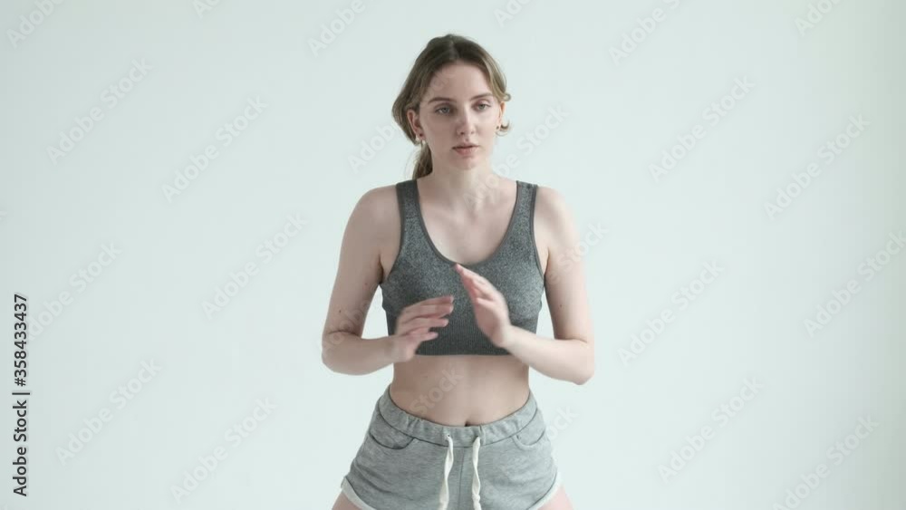 Young fit pretty girl with ponytail in gray top, shorts does exercises on mat in bright room. Doing sports, fitness training on white studio cyclorama. Healthy lifestyle. stretching, leaning forward