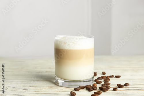 Delicious latte macchiato and coffee beans on white wooden table indoors