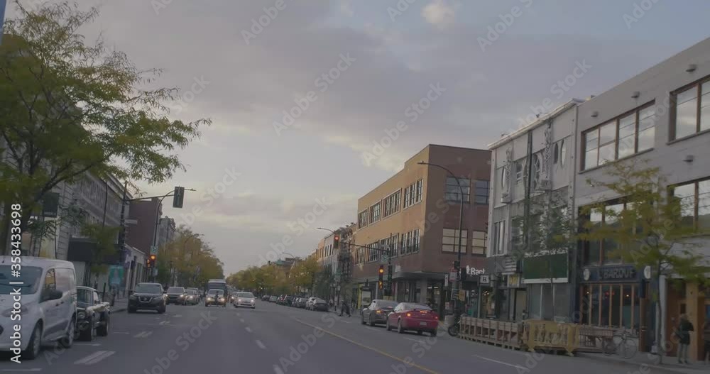Montreal, QC, Canada - April 15, 2017: Buildings facades with cars traffic on wide street lined with trees, filmed while driving on Saint Denis St.