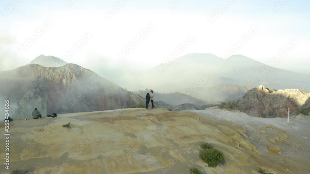 Aerial panning shot of tourists at mountain peak against sky, drone flying near people - East Java, Indonesia Aerial panning shot of tourists at mountain peak against sky, drone flying near people - East Java, Indonesia
