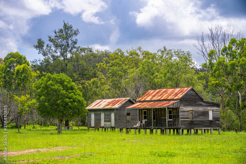 Disused wooden homestead surrounded by grazing field and dramatic stormy sky in Kroombit Tops National Park, Queensland