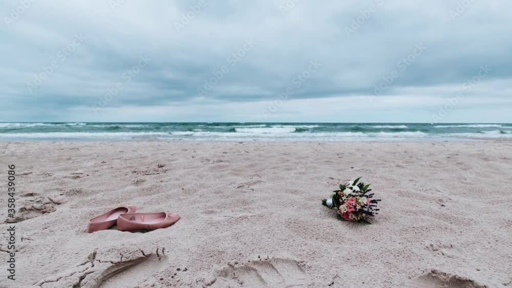Beautiful bouquet with red and white roses and shoes over sand of beach