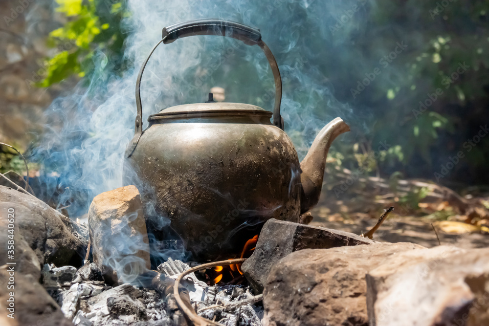 An ancient and antique teapot boiling over a fire flame An ancient and antique teapot boiling over a fire flame
