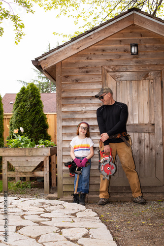 Father and daughter with power tools by back yard shed