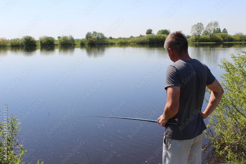 A fisherman stands with a fishing rod and looks at the water A fisherman stands with a fishing rod and looks at the water