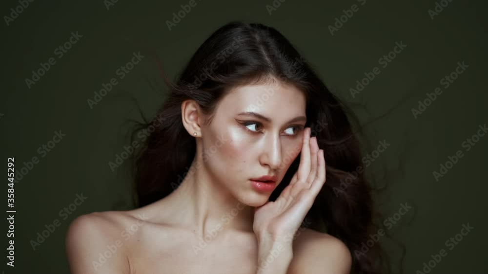A beautiful young woman with long curly black hair, breast portrait, bare shoulders. Beautiful natural skin. Nude makeup. Red lips and graceful hands. Girl poses in studio against an olive background. A beautiful young woman with long curly black hair, breast portrait, bare shoulders. Beautiful natural skin. Nude makeup. Red lips and graceful hands. Girl poses in studio against an olive background.