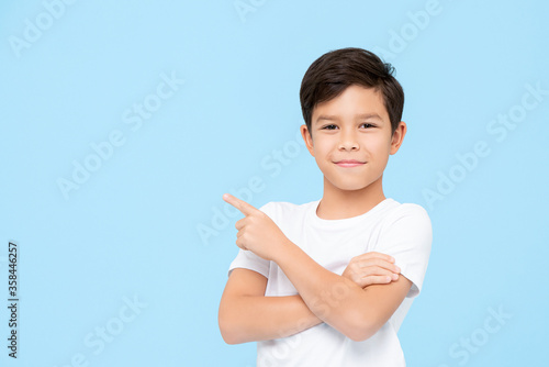 Close-up portrait of smiling young boy pointing finger on blank space beside in blue isolated background photo