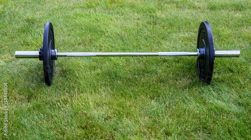 Olympic barbell with black weight plates on a green lawn, ready for an outdoor workout  © knelson20