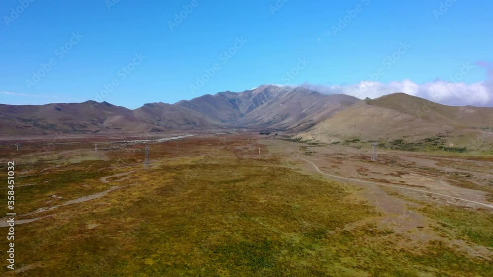 Aerial shot of green landscape with mountains against blue sky, drone flying forward towards mountain range - Lake Tekapo, New Zealand Aerial shot of green landscape with mountains against blue sky, drone flying forward towards mountain range - Lake Tekapo, New Zealand