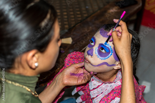 Young woman putting makeup of Catrina in a girl's face