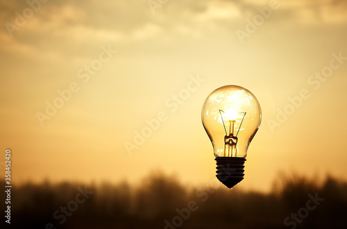 Closeup incandescent light bulb with blur on sky and sunset background.