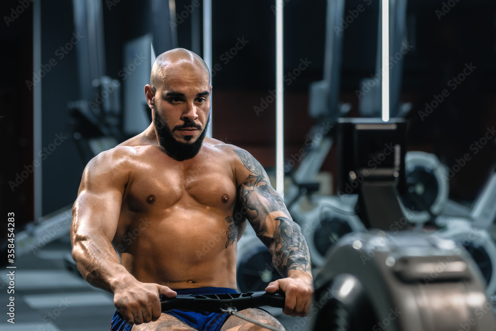 Young muscular man with tattoo doing exercises on rowing machine in gym Young muscular man with tattoo doing exercises on rowing machine in gym