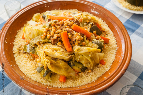 Moroccan typical food shot couscous tagine on a blue squared tablecloth. Dish ingredients chickpeas, carrot, pumpkin, cauliflower, turnip, beef meat and semolina cooked on a big size ceramic plate.