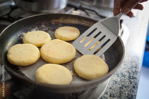 Close up food shot of some circle shaped wheat semolina raw dough pieces on hot pan cooking to make traditional moroccan harsha while a woman hands uses a kitchen palette , a typical breakfast bread.