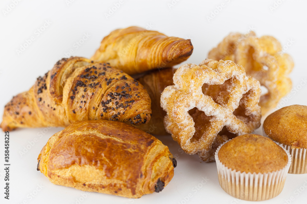 Group of baked sweet pastries on white background. Muffins, pain au chocolat, hazelnut, chocolate and butter croissants and sugar covered fried easter flowers. Spanish and french artisan pastries.