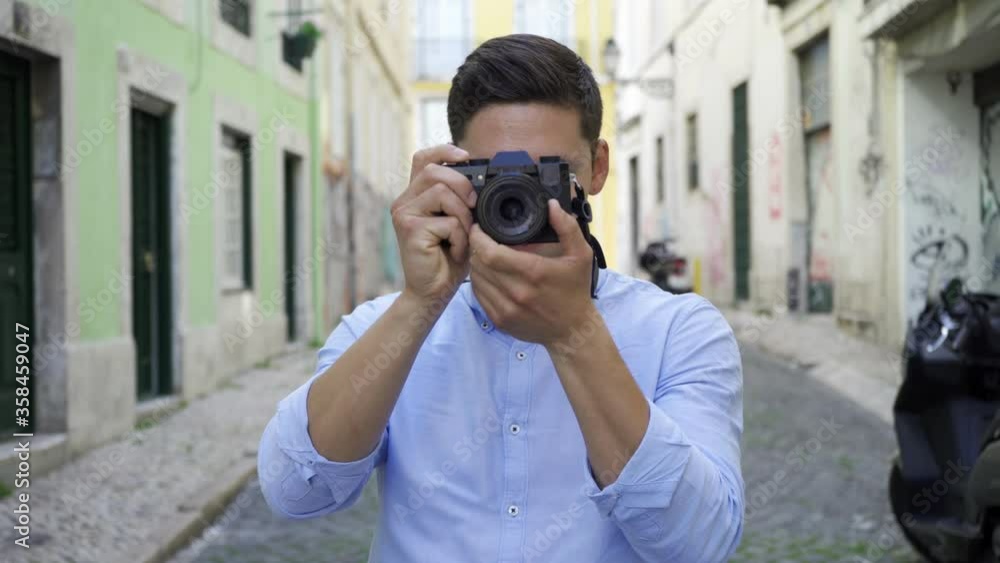 Focused young man taking pictures in old city street, holding and using dslr photo camera. Front view, medium shot. Photographer concept Focused young man taking pictures in old city street, holding and using dslr photo camera. Front view, medium shot. Photographer concept