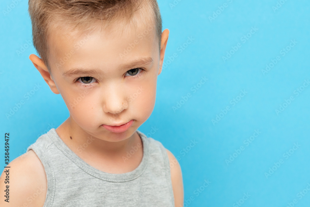 Portrait of little boy with expression on his face with suspicion and surprise on blue background Portrait of little boy with expression on his face with suspicion and surprise on blue background