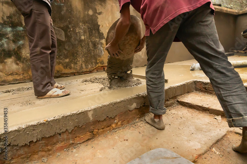 Indian construction labour mixied cement and water and applying cement manually on floor using a bucket. Stock image.