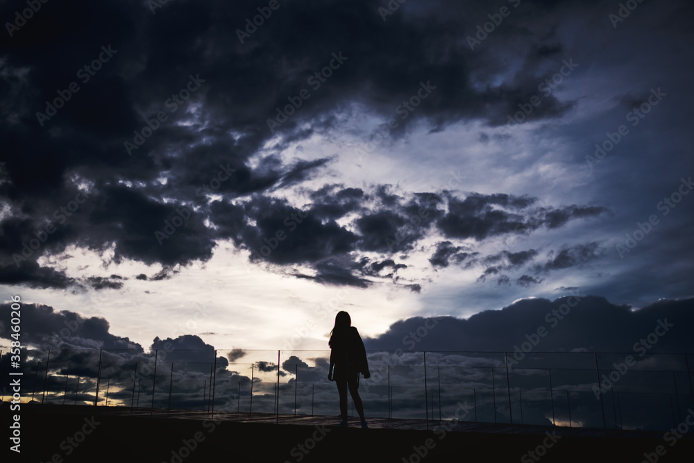Silhouette image of a woman standing alone with sunset cloudy sky