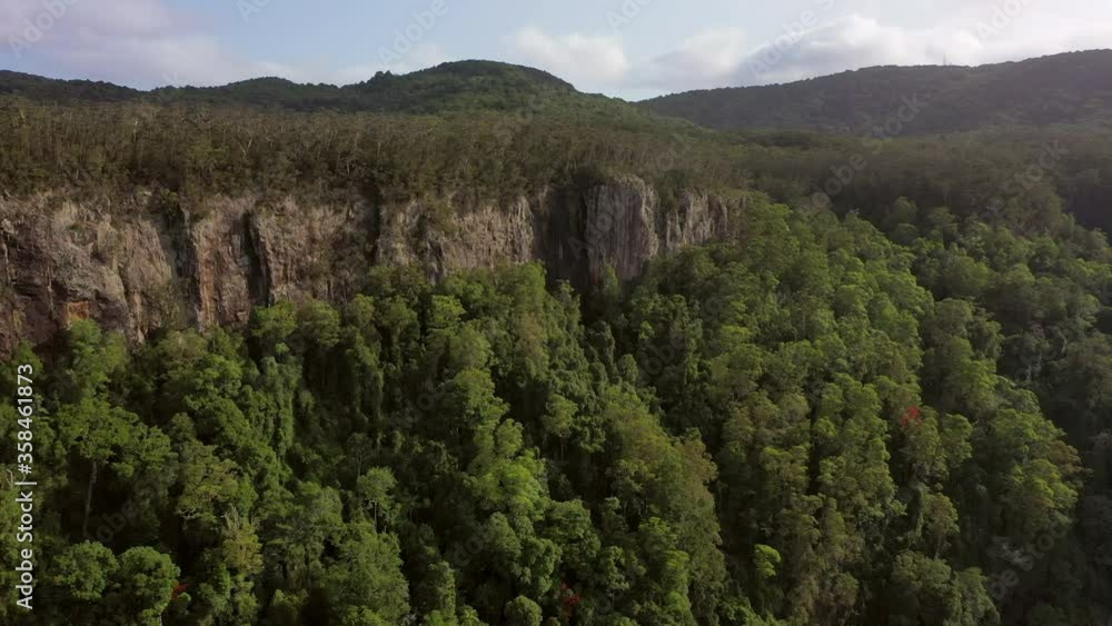 Aerial panning shot of rocky cliff in green forest against sky, drone flying forward over Springbrook National Park on sunny day Aerial panning shot of rocky cliff in green forest against sky, drone flying forward over Springbrook National Park on sunny day