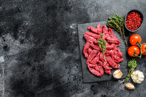Raw meat cut into thin strips for beef Stroganoff. Black background. Top view. Copy space
