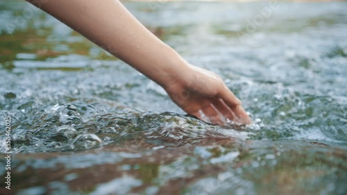 Hand touching water in the forest river or lake. People travel enjoying nature and life concept. photo
