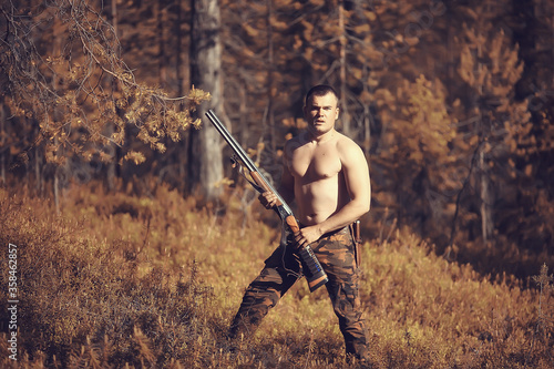 hunting man / hunter with a gun hunting in the autumn forest, yellow trees landscape in the taiga photo