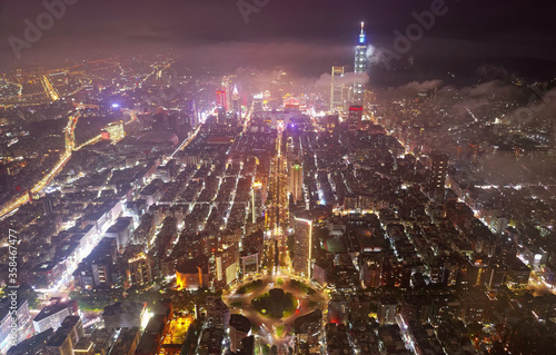 Aerial night skyline of Taipei Downtown viewed from above the circular intersection of Ren'ai & Dunhua Roads, with towers among skyscrapers standing high into clouds in Xinyi Commercial District
