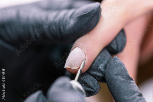 Close-up shot of hardware manicure in a beauty salon. Manicurist is applying electric nail file drill to manicure on female fingers.