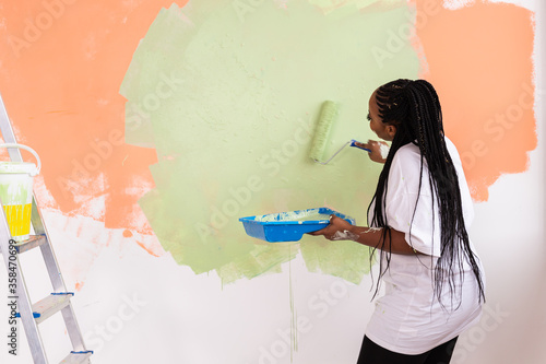 Quadro em tela Pretty smiling african american woman painting interior wall of home with paint roller