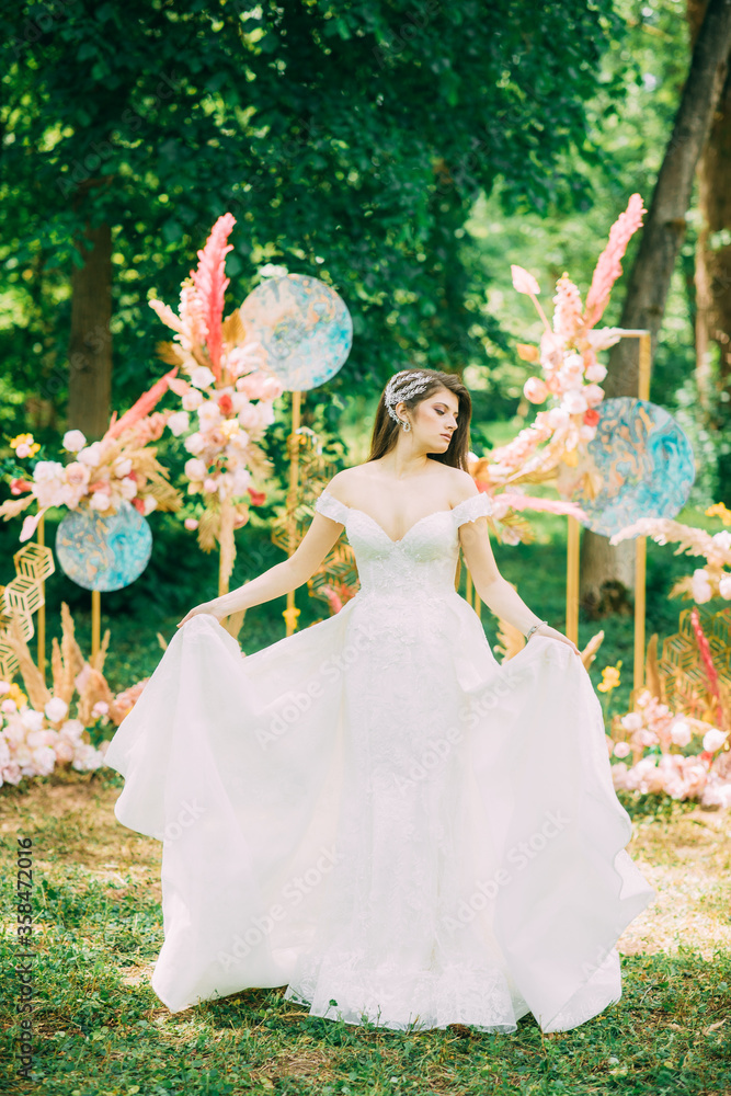 Beautiful caucasian brunette bride is standing near the archway made of blue and pink hydrangea outdoors